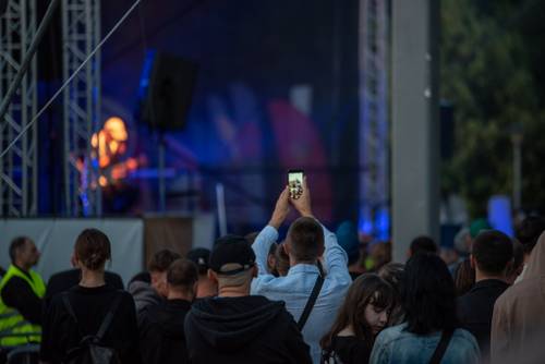 Punliczność oglądająca koncert, jeden z widzów wykonuje zdjęcie telefonem