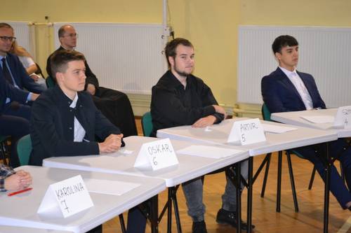 Uczestnicy konkursu siedzący przy stoliakch.