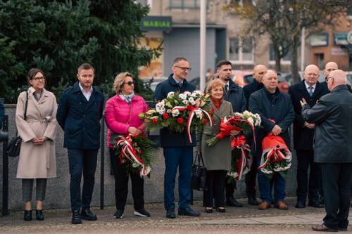 Przedstawiciele władz lokalnych stojący przed tłumem z kwiatami.