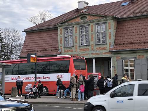 Widok ruchliwej ulicy, osoby kłębiące się przy krwiobusie, chcące oddać krew.