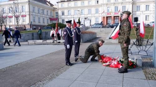 Goście składają kwiaty pod pomnikiem Nike. Z kwiatami przedstawiciele służb mundurowych.
