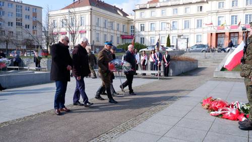 Goście składają kwiaty pod pomnikiem Nike. Z kwiatami przedstawiciele organizacji kombatanckich.