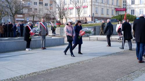 Goście składają kwiaty pod pomnikiem Nike. Z kwiatami przedstawicielki organizacji pozarządowych.
