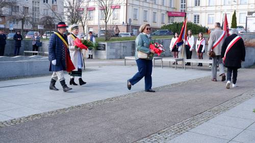 Goście składają kwiaty pod pomnikiem Nike. Z kwiatami przedstawicielka organizacji pozarządowej i związku Kaszubów w strojach ludowych..