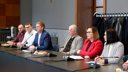 Grupa osób siedzących przy stole konferencyjnym podczas spotkania dotyczącego organizacji ruchu, widoczny mikrofon i notatki.