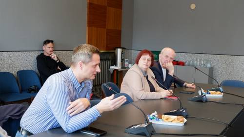Dyskusja podczas spotkania – jedna z osób zabiera głos, pozostali uczestnicy słuchają; na stole widoczne mikrofony i poczęstunek.