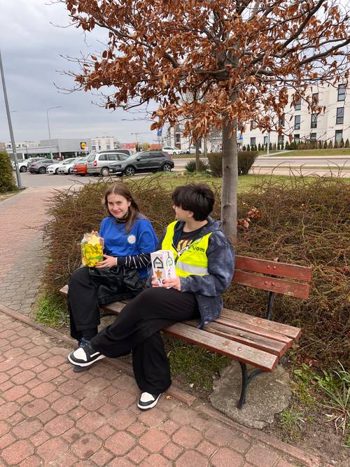 Wolontariusze podczas kwesty siedzą na ławeczce miejskiej.