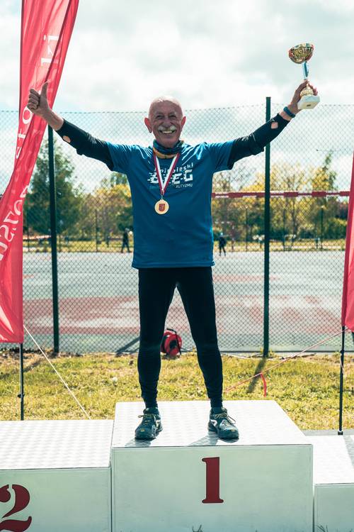 Najstarszy uczestnik z pucharem stoi na podium.