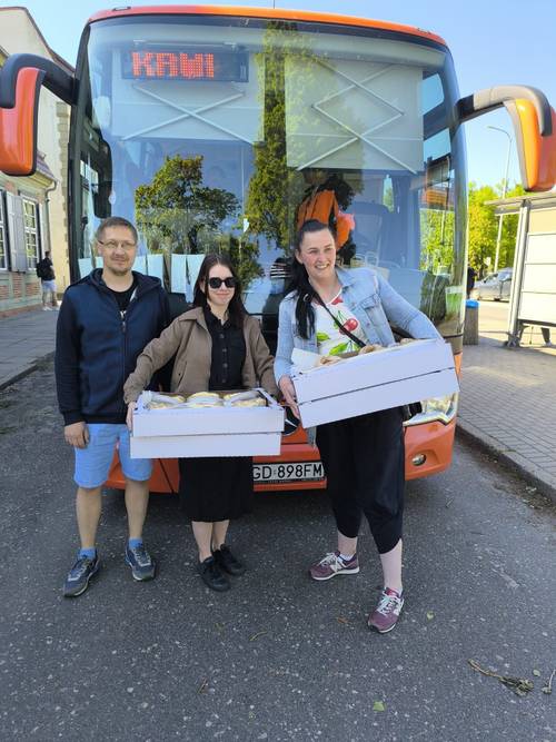 Organizatorzy i partnerzy stoją przed autobusem. Dwie kobiety trzymają pudła ze słodkościami.