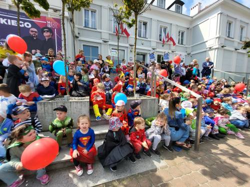Dzieci w strojach superbohaterów siedzą na schodach Urzędu Miasta.
