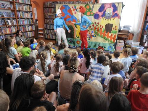 Przedstawienie w bibliotece, dzieci siedzą na podłodze, przed nimi Smerfy, w tym Papa Smerf