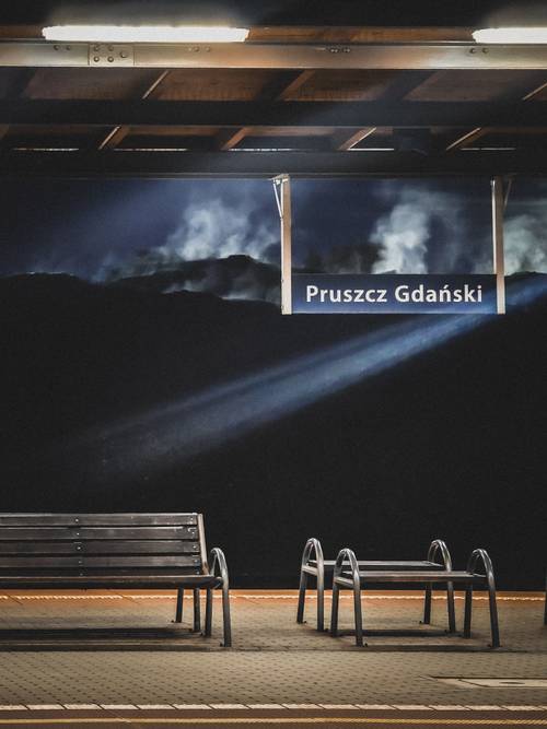 Smuga światła na peronie. Napis Pruszcz Gdański i ławeczki.