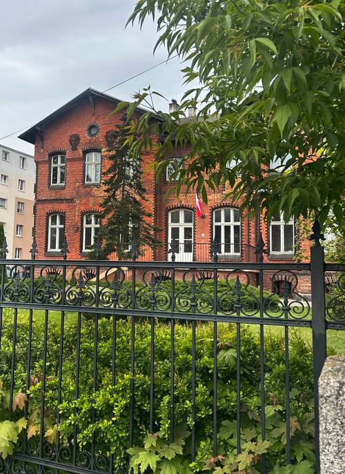 Ceglany budynek zza płotu.