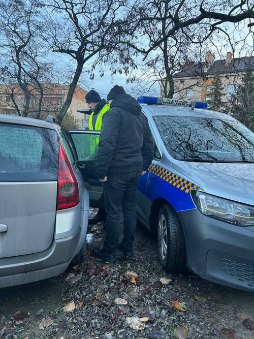 Dwie postacie stojące przy aucie z otwartymi drzwiami