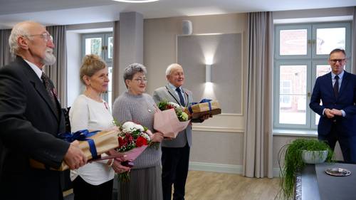 Dwie pary jubilatów z kwiatami i prezentami