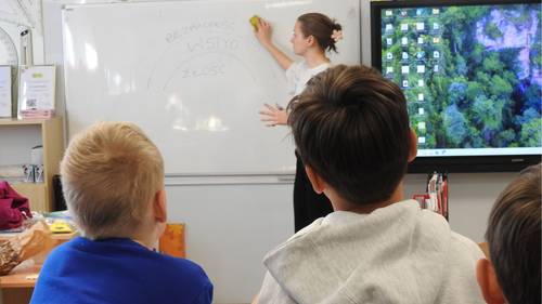 Trójka uczniów patrzy na panią, która stoi przy tablicy