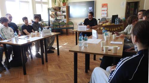 Grupy uczniów siedzą przy stole i prowadzą dyskusję