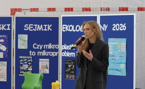 Kobieta z mikrofonem w ręku stoi przed tablicą z napisem Sejmik Ekologiczny 2026