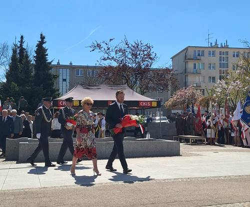 Uczestnicy uroczystości idą z wiązankami kwiatów