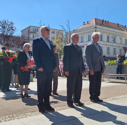 Uczestnicy obchodów stoją pod pomnikiem Nike