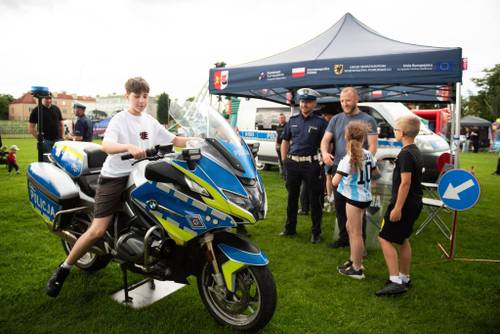 Chłopiec siedzi na policyjnym motocyklu, obok stoi dwójka dzieci, mężczyzna i policjant