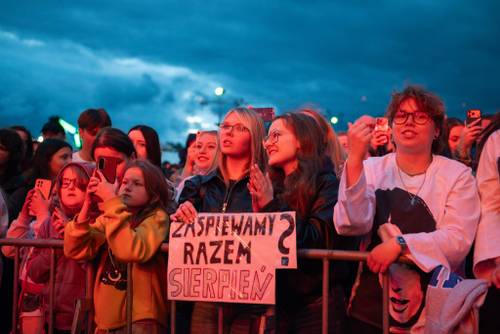 Grupa osób za barierkami z kartką z napisem