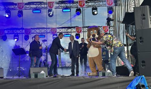 Burmistrz Pruszcza ściska rękę starszemu panu na scenie, obok lewe maskotka