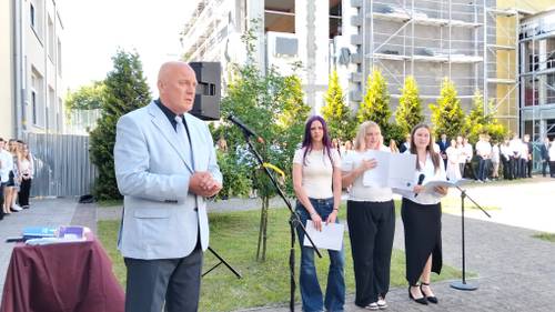 Dyrektor szkoły przemawia do mikrofonu, z tyłu stoją uczniowie