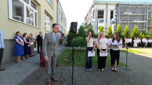 Zastępca burmistrza przemawia do mikrofonu, z tyłu uczniowie i nauczyciele