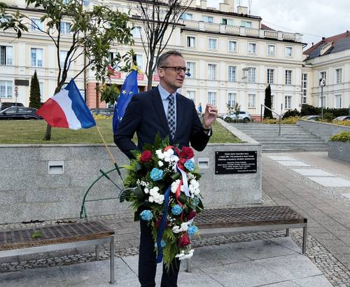 Burmistrz Pruszcza Gdańskiego z kwiatami w ręku stoi przy tablicy pamiątkowej
