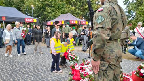 Trójka przedszkolaków z panią składają kwiaty