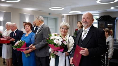 Zbliżenie na trzy pary jubilatów z kwiatami