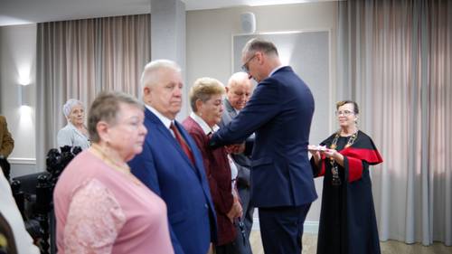 Burmistrz Pruszcza przypina starszej pani medal do klapy marynarki, obok stoją pozostali jubilaci