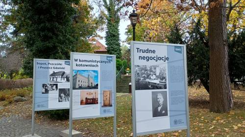 Widok na trzy plansze stojące przy alejce z drzewami