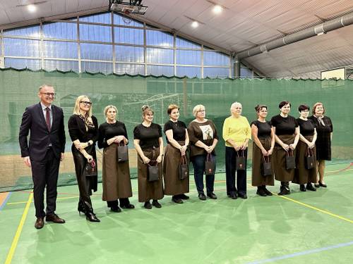 Grupa pań stoi w szeregu z torebkami w rękach, obok nich burmistrz