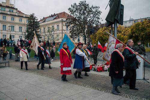 Uczestnicy ze sztandarami przechodzący przed pomnikiem.