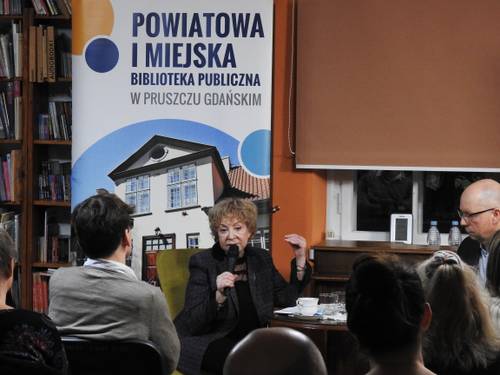 Autorka udzielająca odpowiedzi na tle grafiku biblioteki